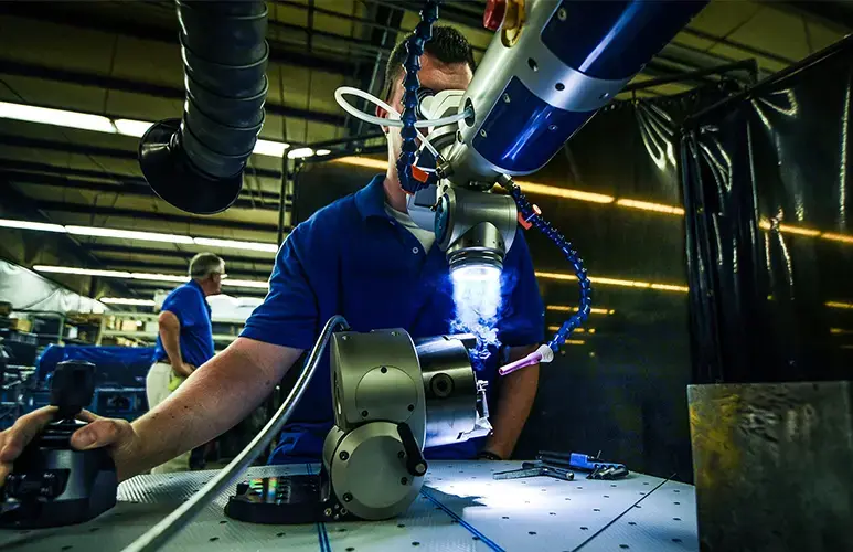 Person operating a robotic arm in a factory setting, with tools and machinery visible.