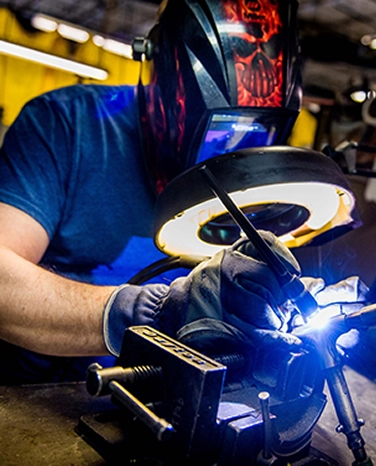 Person wearing a welding mask, using a welding torch in a workshop.