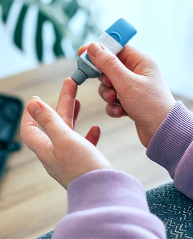Person using a lancet device to prick their finger for a blood glucose test.