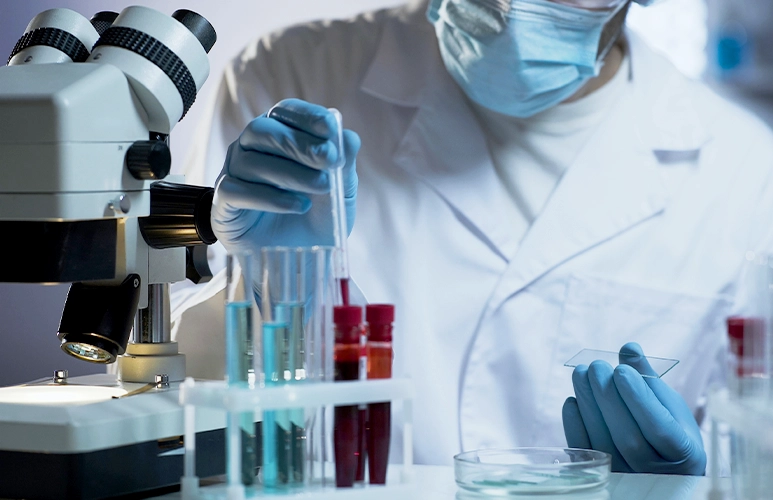 Scientist in a lab coat conducts an experiment with test tubes beside a microscope.