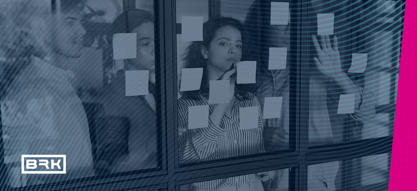 Four people stand behind glass covered with sticky notes, appearing to brainstorm or discuss ideas.