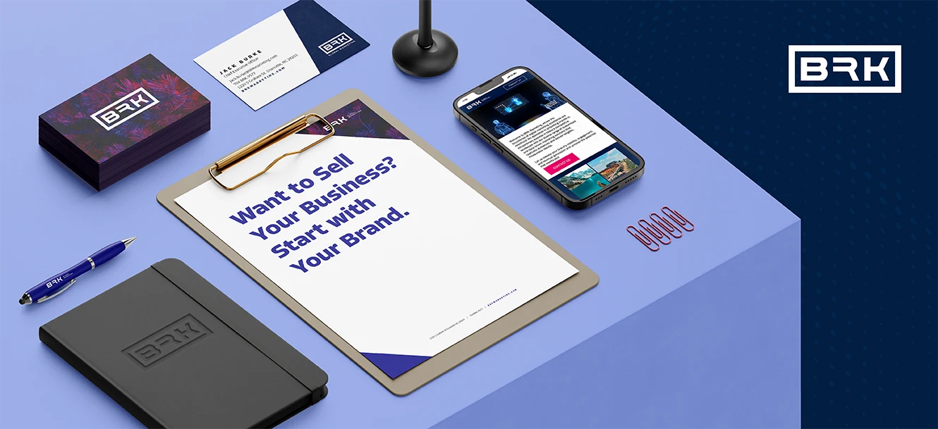 Clipboard reading “Want to Sell Your Business? Start with Your Brand.” on a desk with office supplies and a phone.