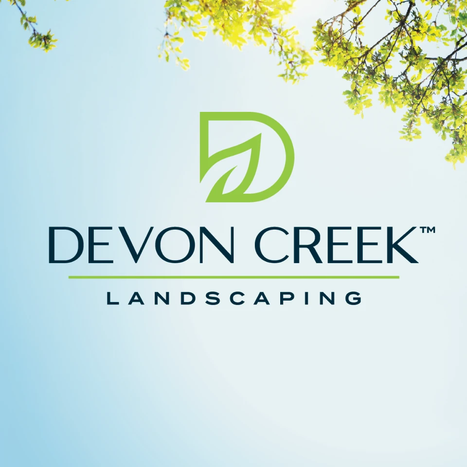 Devon Creek Landscaping logo with green leaves and tree branches against a clear blue sky.