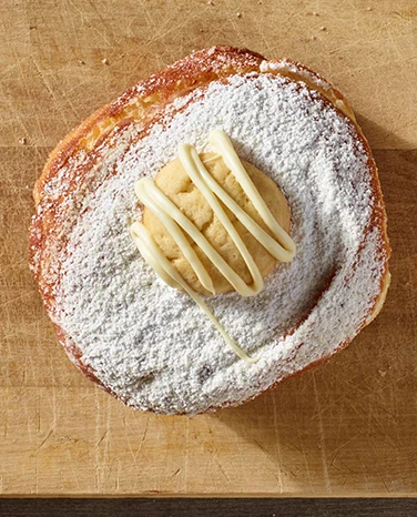 A pastry dusted with powdered sugar, topped with a cookie and drizzled with white icing.