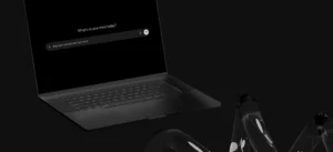 A black laptop with a dark screen displays a search box that reads, “What’s on your mind today?” The background and surrounding objects are also dark-colored.